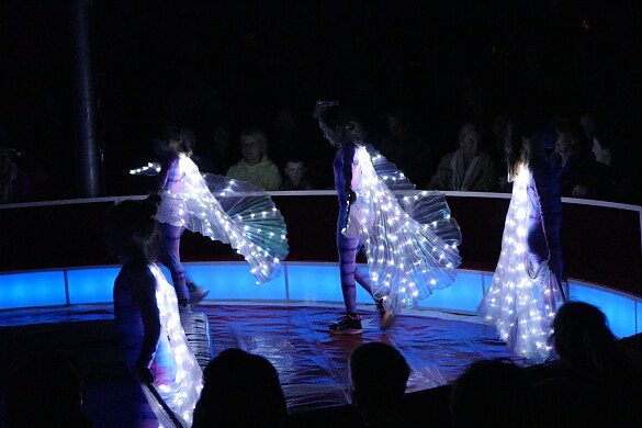 3 Tänzerinnen in beleuchteten Kleidern gehen über die Bühne