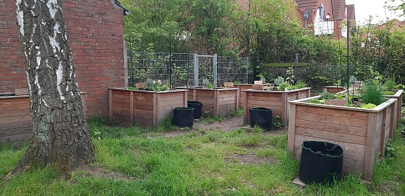 Zu sehen sind 8 Hochbeete, die im hinteren Garten der Schule stehen. Jede Klasse hat ein Hochbeet, um welches sich die Kinder kümmern.