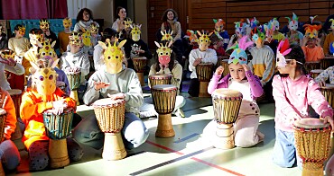 Kinder mit Giraffen- und Vogelmasken auf dem Kopf während des Trommelprojekts