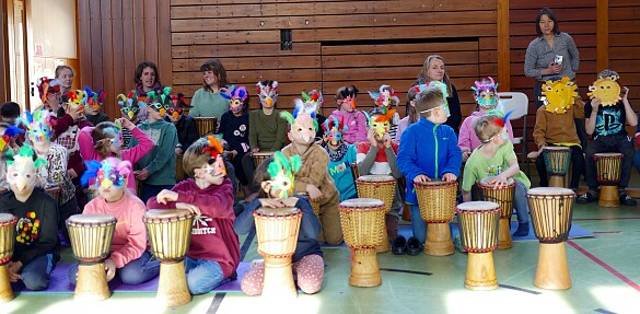 Kinder mit Vogel- und Löwenmasken auf dem Kopf während des Trommelprojekts